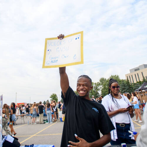 student holds sign for GVSU gospel choir table at Campus Life Night